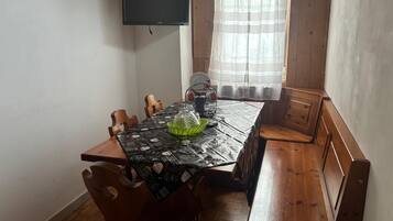 A dining area with a table, chairs, a television mounted on the wall, and a window with curtains.