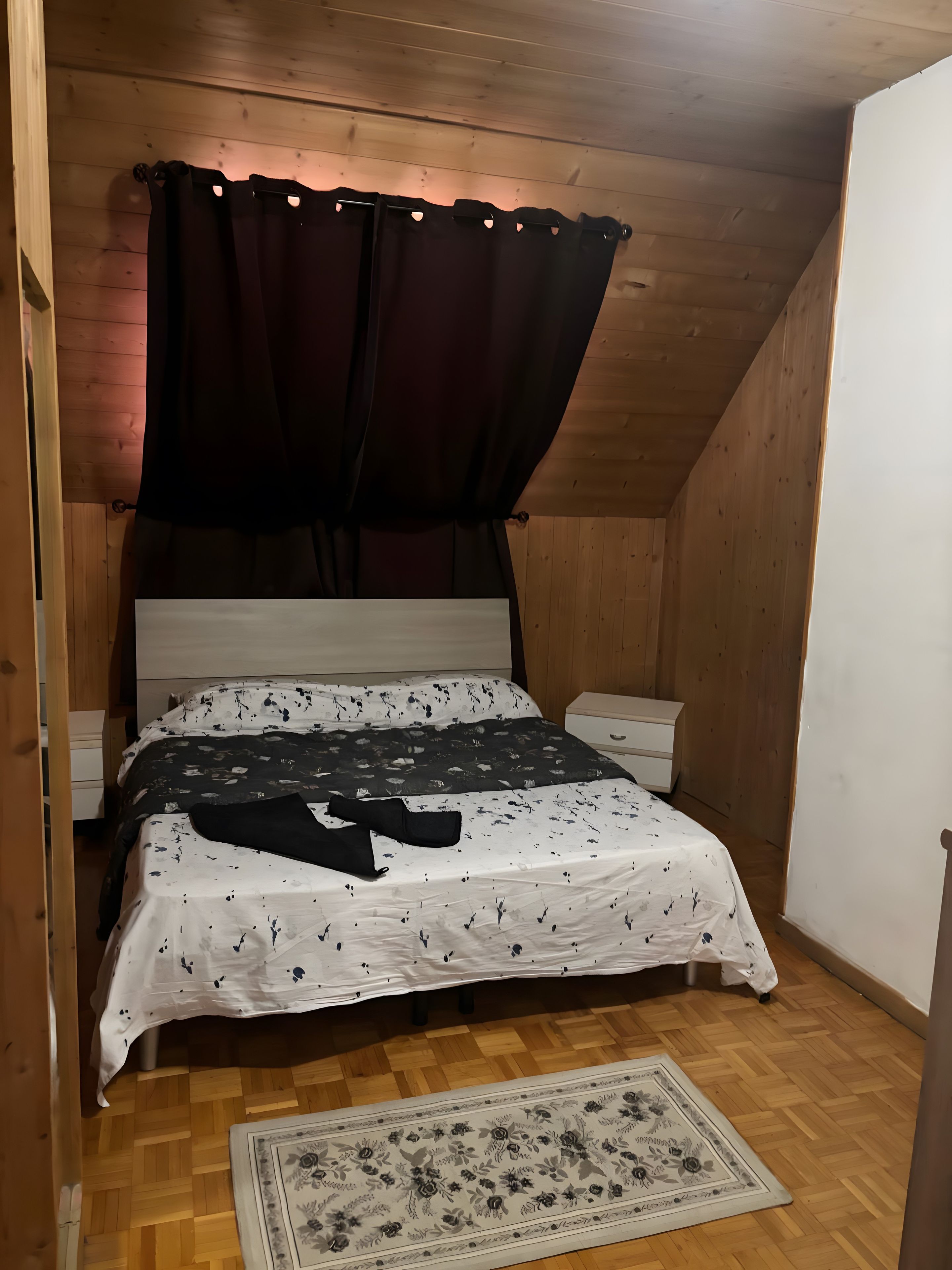 Ett sovrum med ett träpanelat tak, en säng med ett blommigt överkast, ett sängbord och ett litet bord vid sängen.
