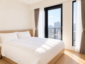 Ett hotellrum med en stor säng, utsikt över staden genom en skjutdörr och en balkong med gardiner.
