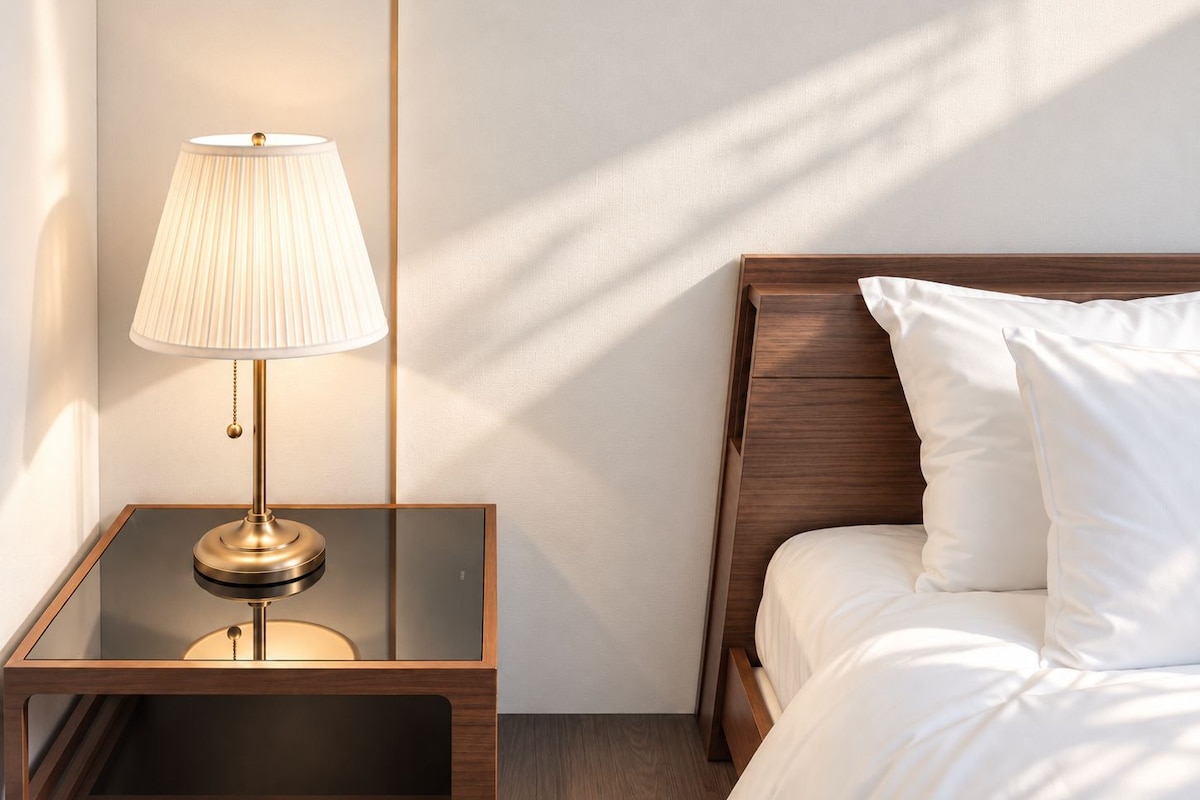 Ett hotellrum med ett nattduksbord, en lampa, en säng med vita sängkläder och en sänggavel i trä.