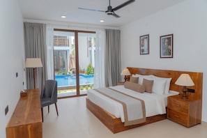 Una habitación de hotel con cama, mesitas de noche, escritorio, silla, ventilador de techo y vista a una piscina.