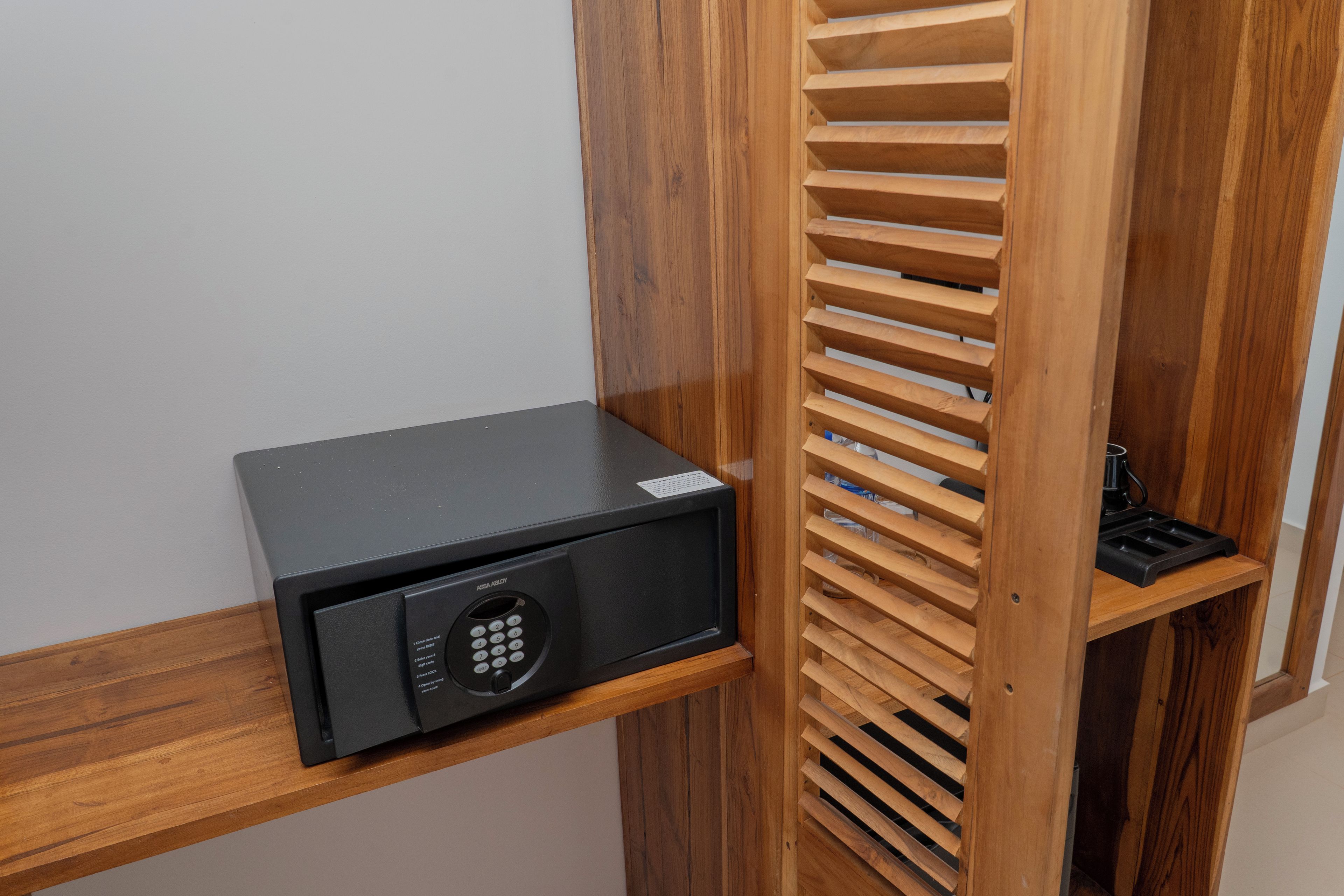 A black security keypad on a wooden shelf, a wooden slatted partition, and a black object on a lower shelf.