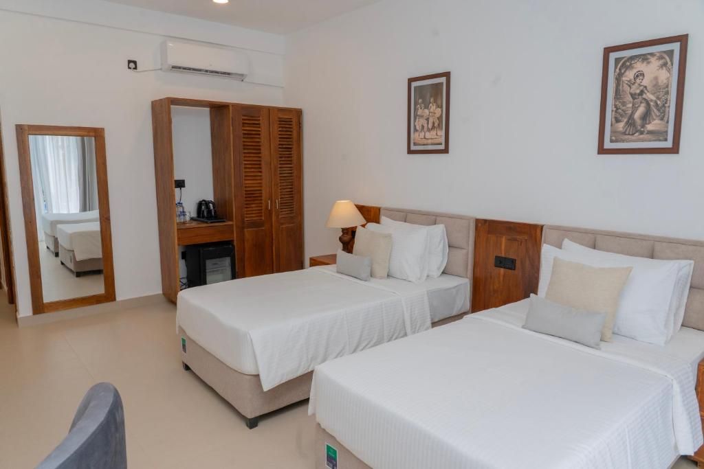 A hotel room with two beds, a wardrobe, a mirror, and a wall-mounted lamp.