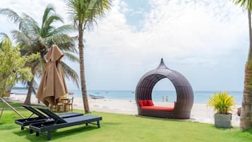A beachside lounge area with a circular seating structure, a sun lounger, and a palm tree.