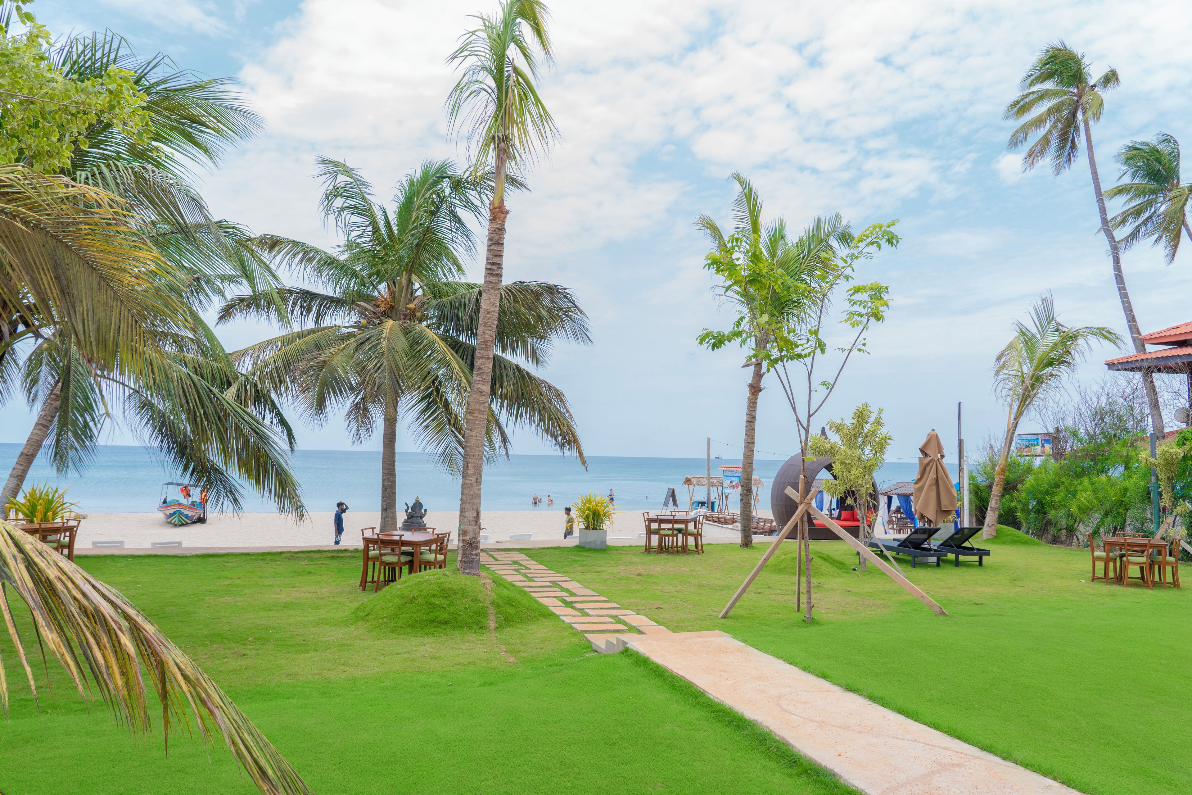 A tropical resort with a clear view of the beach, palm trees, and a dining area with outdoor seating.