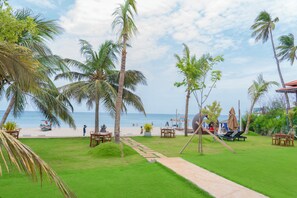 A tropical resort with a clear view of the beach, palm trees, and a dining area with outdoor seating.