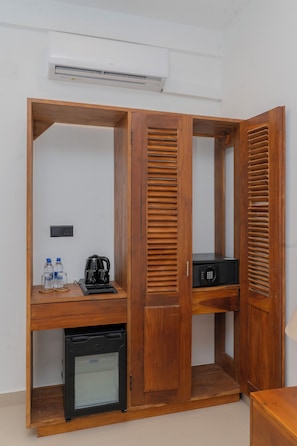 Una habitación con un armario de madera, un refrigerador pequeño, una cafetera y un microondas.