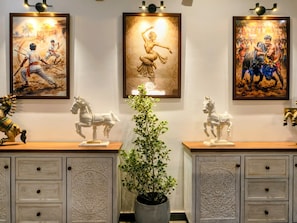 Una habitación con dos armarios de madera, cada uno con una estatua de caballo blanco encima. Hay tres obras de arte enmarcadas en la pared, y una planta en maceta en el centro.