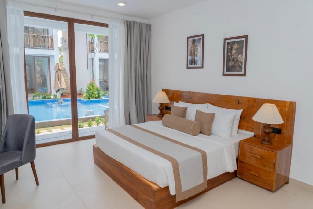Ein Hotelzimmer mit einem großen Bett, einem Sessel, einem Nachttisch und Blick auf einen Swimmingpool.