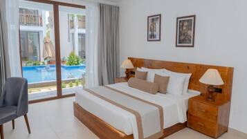 Ein Hotelzimmer mit einem großen Bett, einem Sessel, einem Nachttisch und Blick auf einen Swimmingpool.