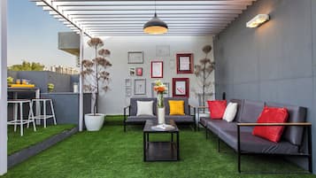 A modern outdoor seating area with a sofa, chairs, and a coffee table. There are framed pictures on the wall and a hanging light fixture.