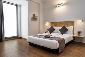 Habitación de hotel moderna con una cama grande, mesitas de noche, un cabecero de madera y una ventana con cortinas.