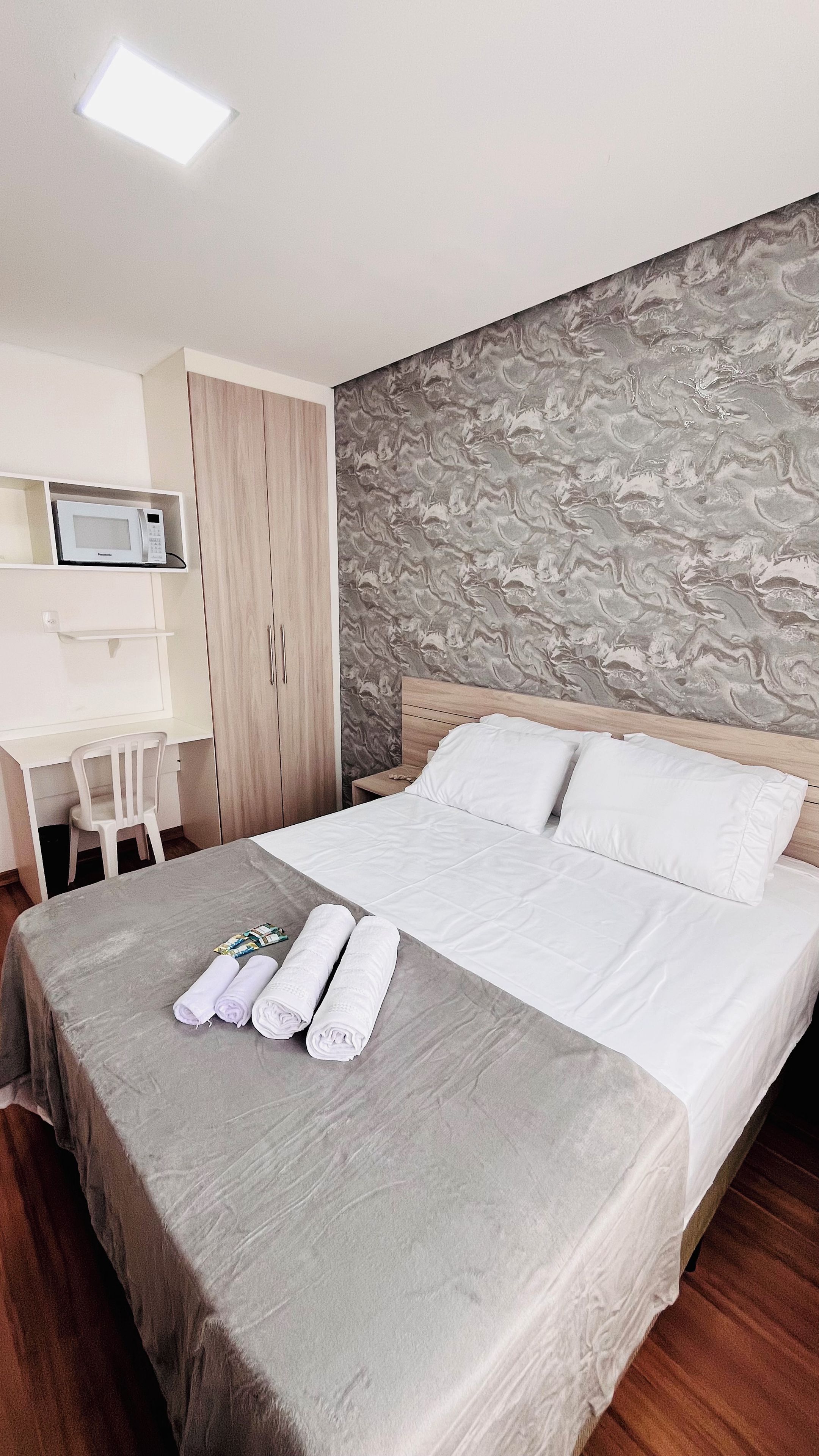 Habitación de hotel con cama, escritorio con silla, microondas y armario.
