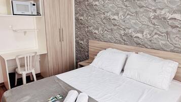 Habitación de hotel con cama, escritorio con silla, microondas y armario.