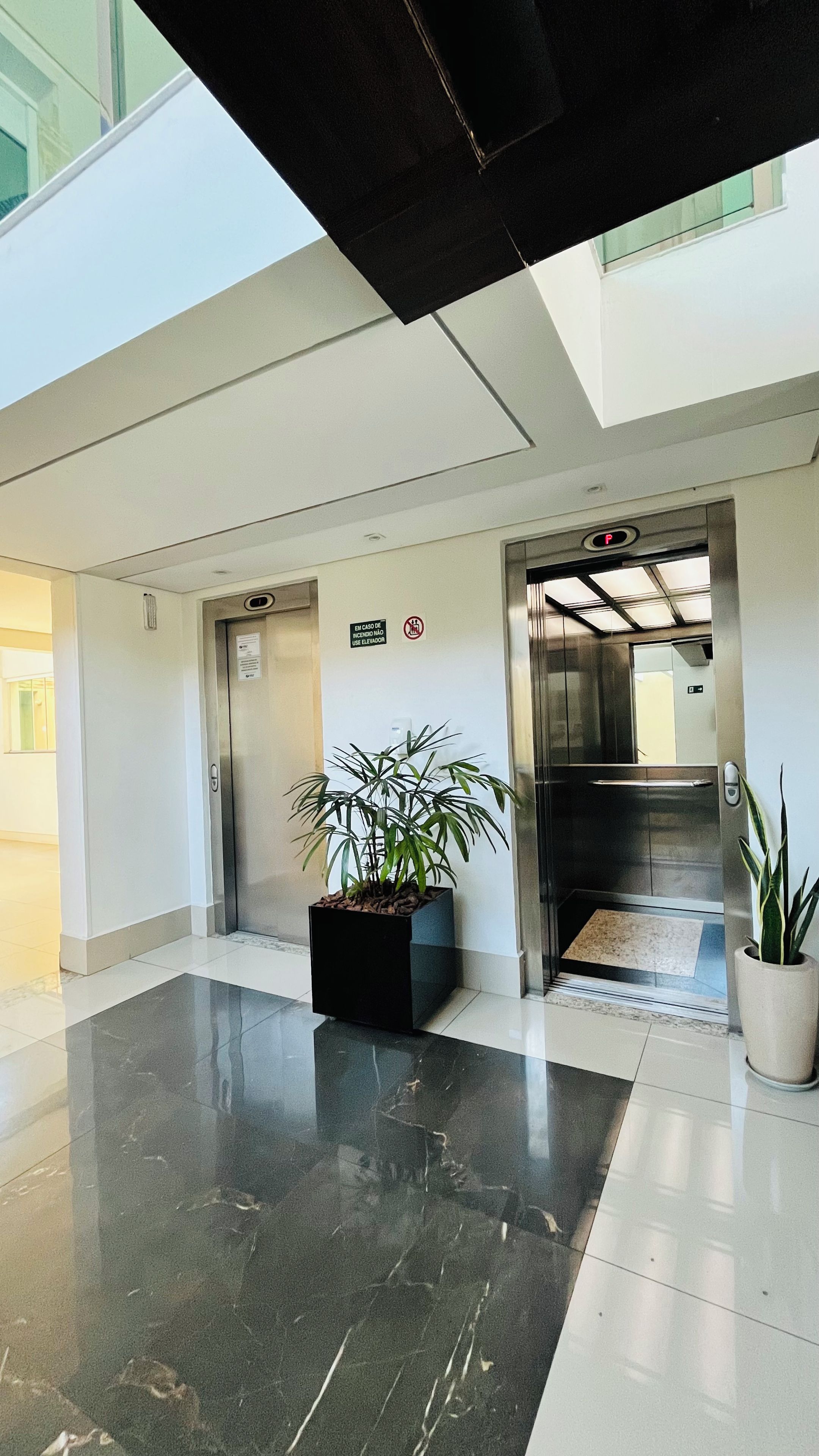 A modern lobby with a polished floor, two elevators, and potted plants.