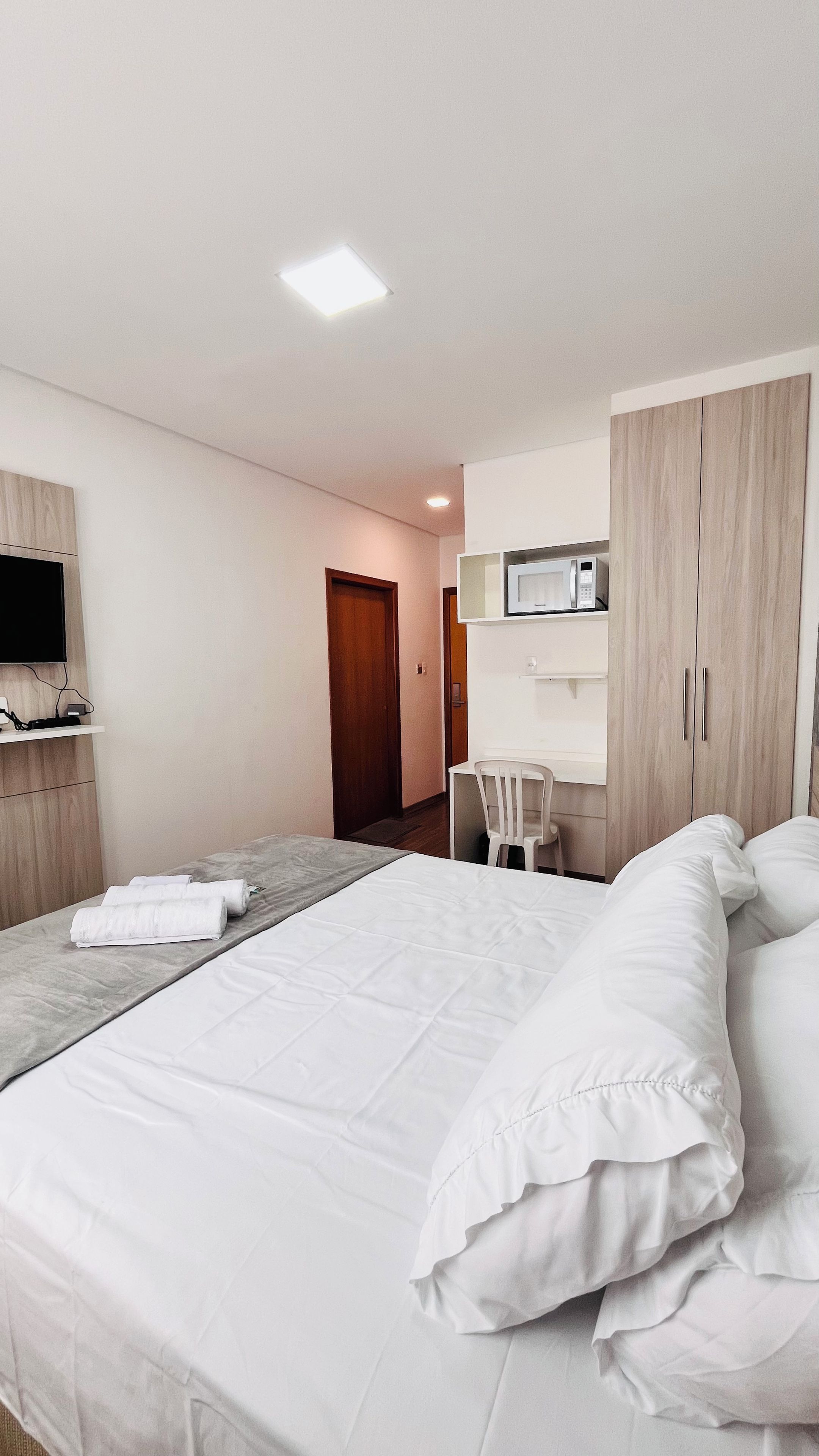 A hotel room with a bed, a desk, a chair, a wardrobe, and a television.