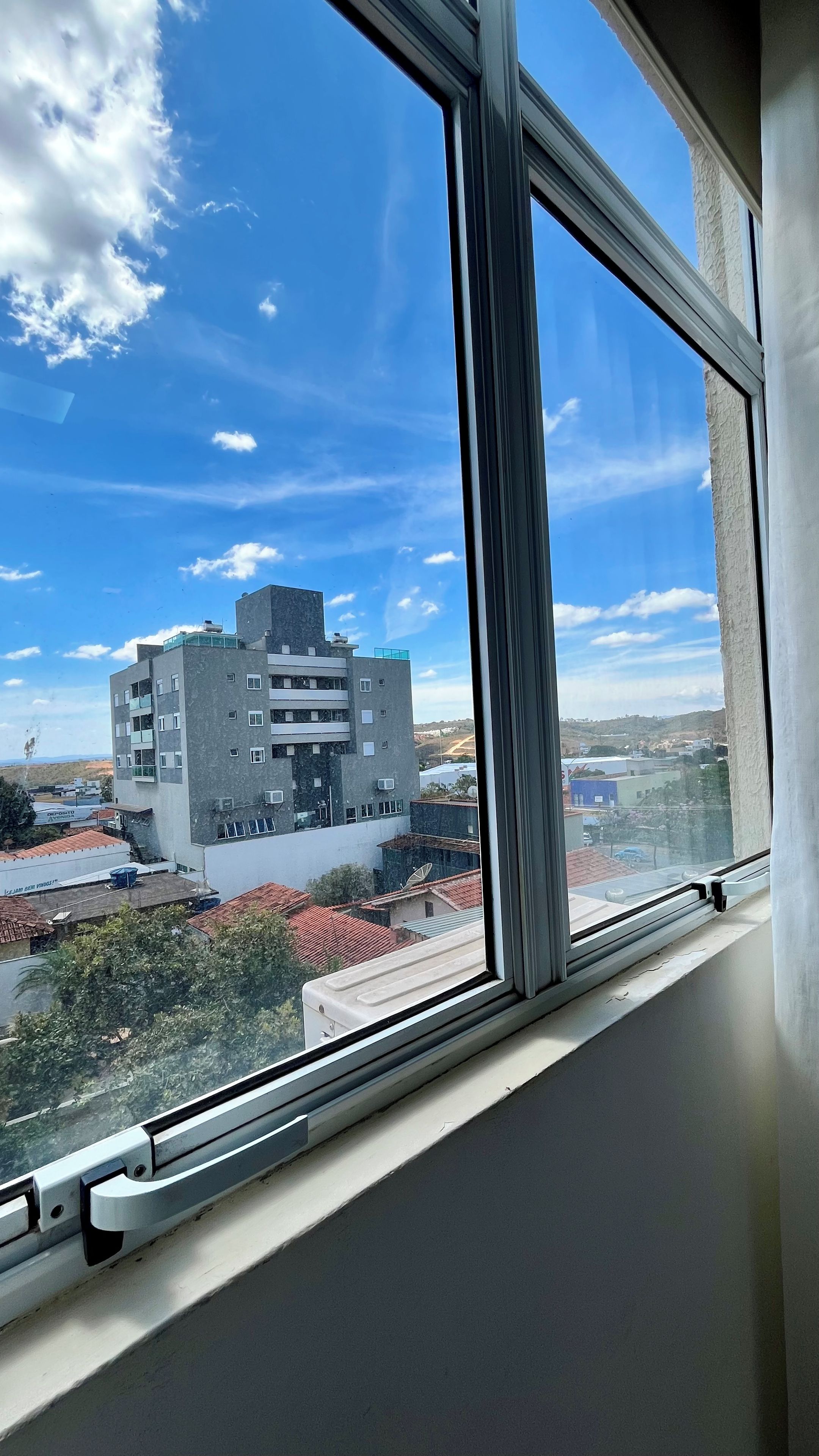 A window with a view of a multi-story building with a flat roof and several windows.