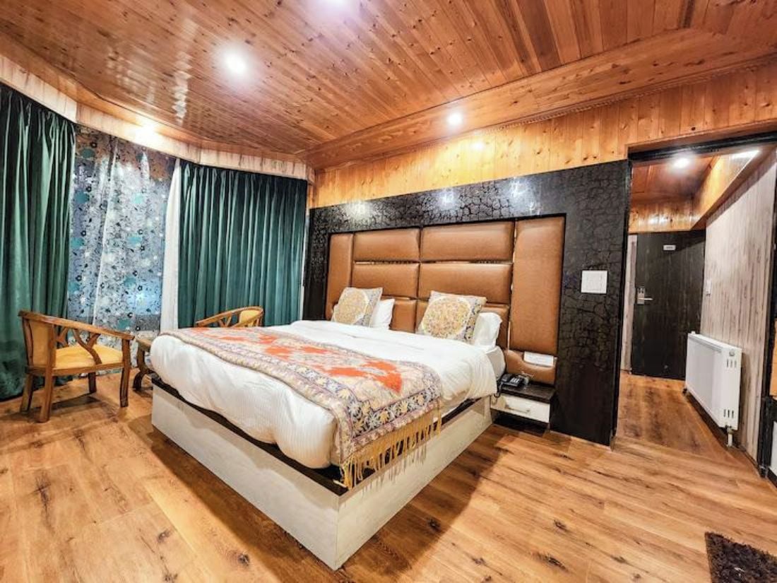 A bedroom with a large bed, wooden flooring, a headboard, and a chair.
