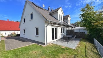 Una casa de dos pisos con patio, techo rojo y fachada blanca.