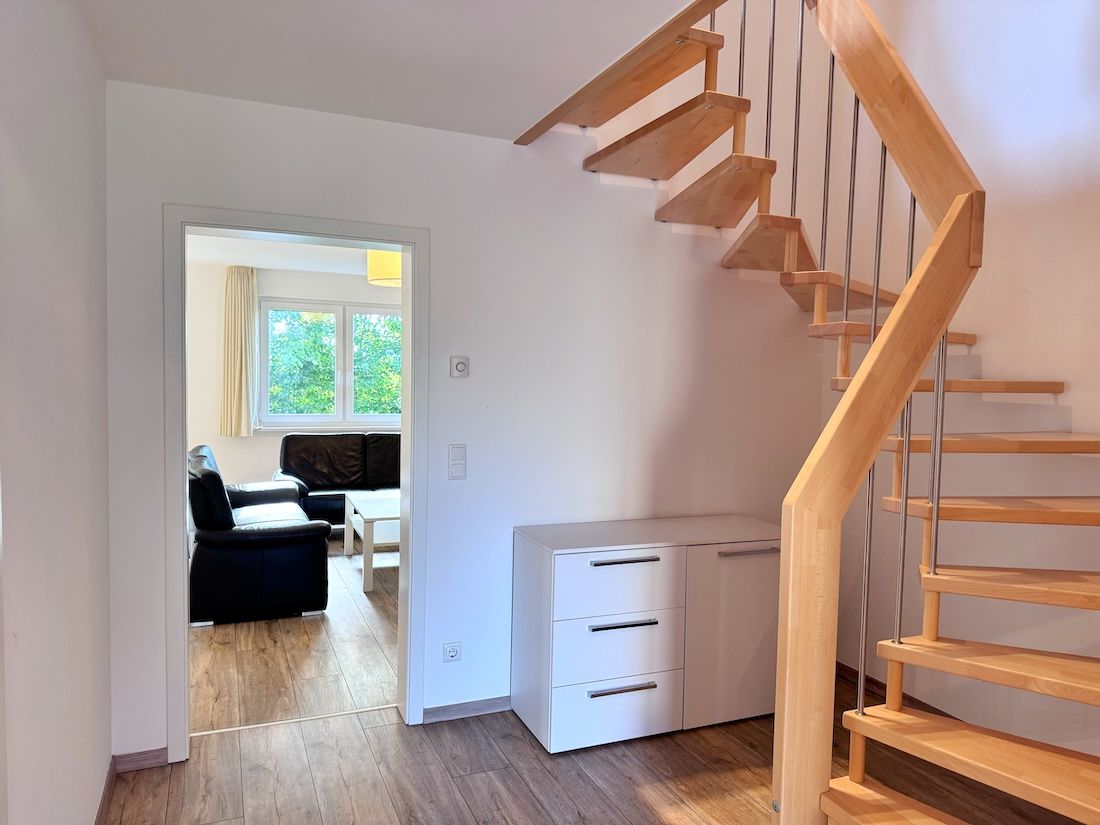 A staircase leading to a second floor, a white cabinet with drawers, and a view into a living area with a sofa and a table.