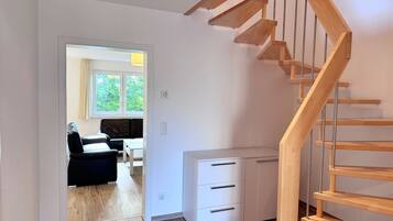A staircase leading to a second floor, a white cabinet with drawers, and a view into a living area with a sofa and a table.