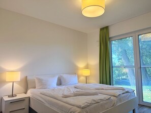 Una habitación de hotel con una cama, dos lámparas de noche, una mesita de noche y una ventana con cortinas.