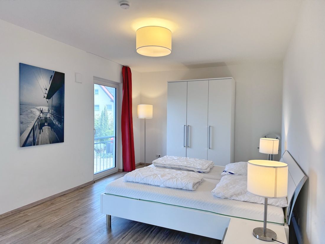 Ein modernes Schlafzimmer mit Bett, Nachttischlampen, einem Kleiderschrank und einem großen Fenster mit Aussicht.