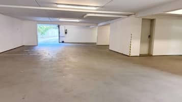 A spacious indoor parking area with concrete floors and white walls, featuring a single door and a visible exit.