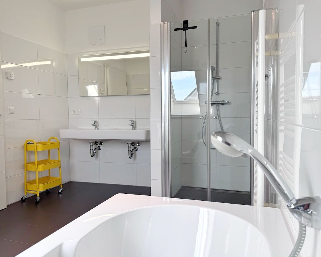 Une salle de bain moderne avec une grande baignoire, une cabine de douche en verre et un chariot de nettoyage jaune.
