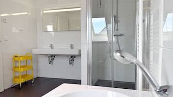 Une salle de bain moderne avec une grande baignoire, une cabine de douche en verre et un chariot de nettoyage jaune.