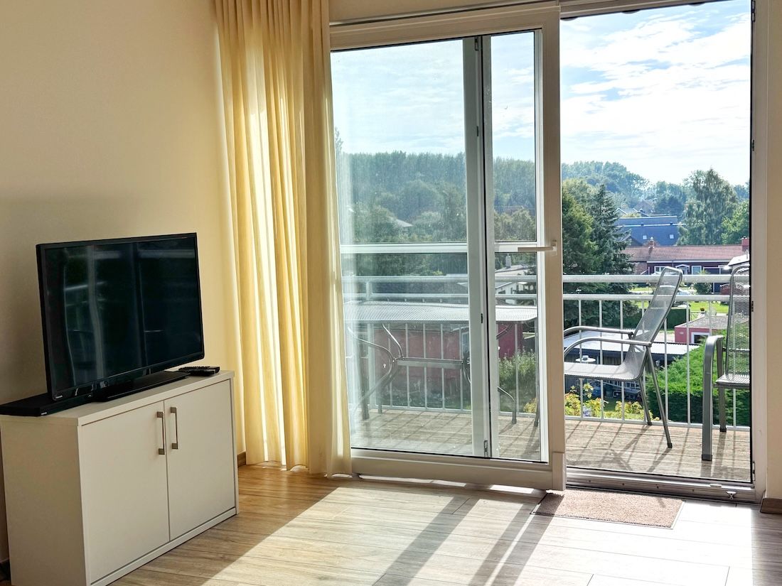A room with a sliding glass door leading to a balcony, a television on a cabinet, and a view of a residential area.