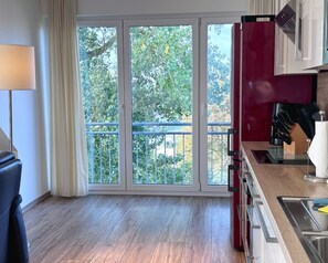 A modern kitchen with a sliding glass door leading to a balcony, a red refrigerator, and a sink with a wooden countertop. - My Glowe - DG on the left (Glowe)
