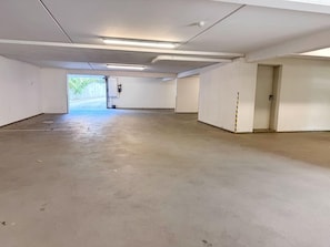 A spacious indoor parking area with concrete floors and white walls, featuring a single door and a visible exit. - My Glowe - 1st floor, left (Glowe)