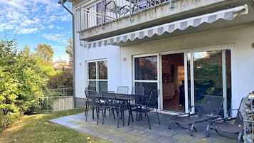 A two-story house with a balcony, a patio with a table and chairs, and a garden area.