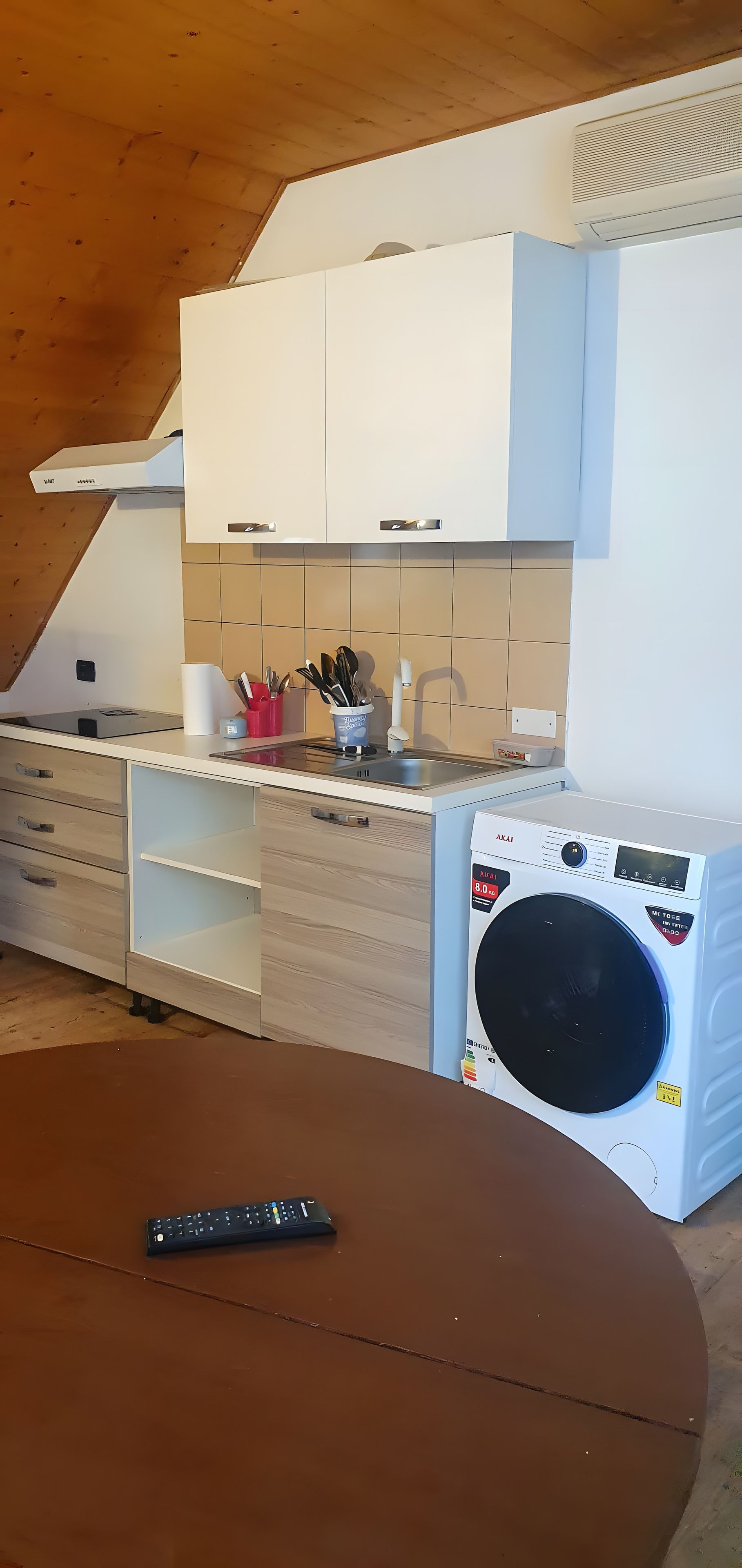 A compact kitchen with a washing machine, a dining table, and a remote control.