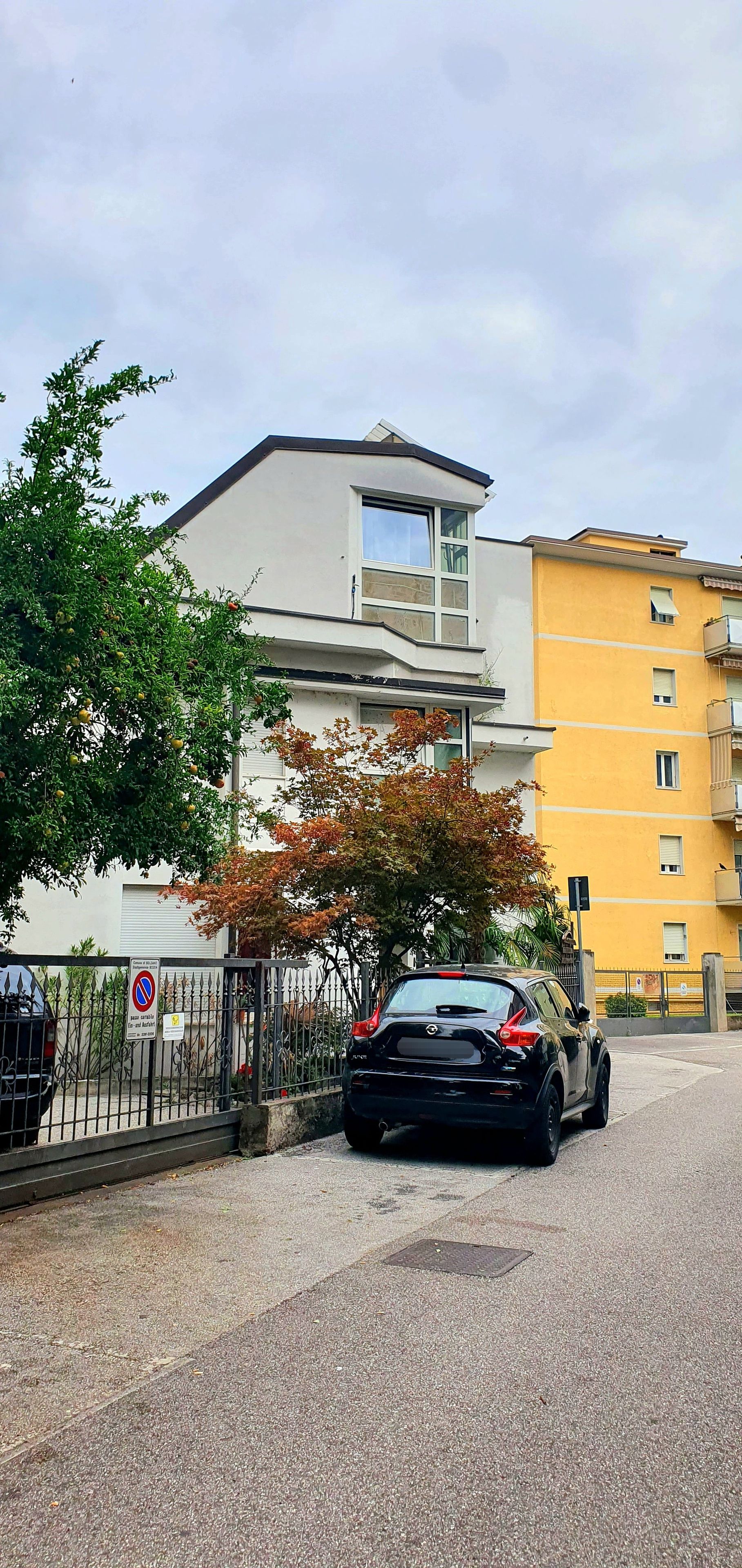 A parking area with a black car, a building with a white facade, and a yellow building in the background.