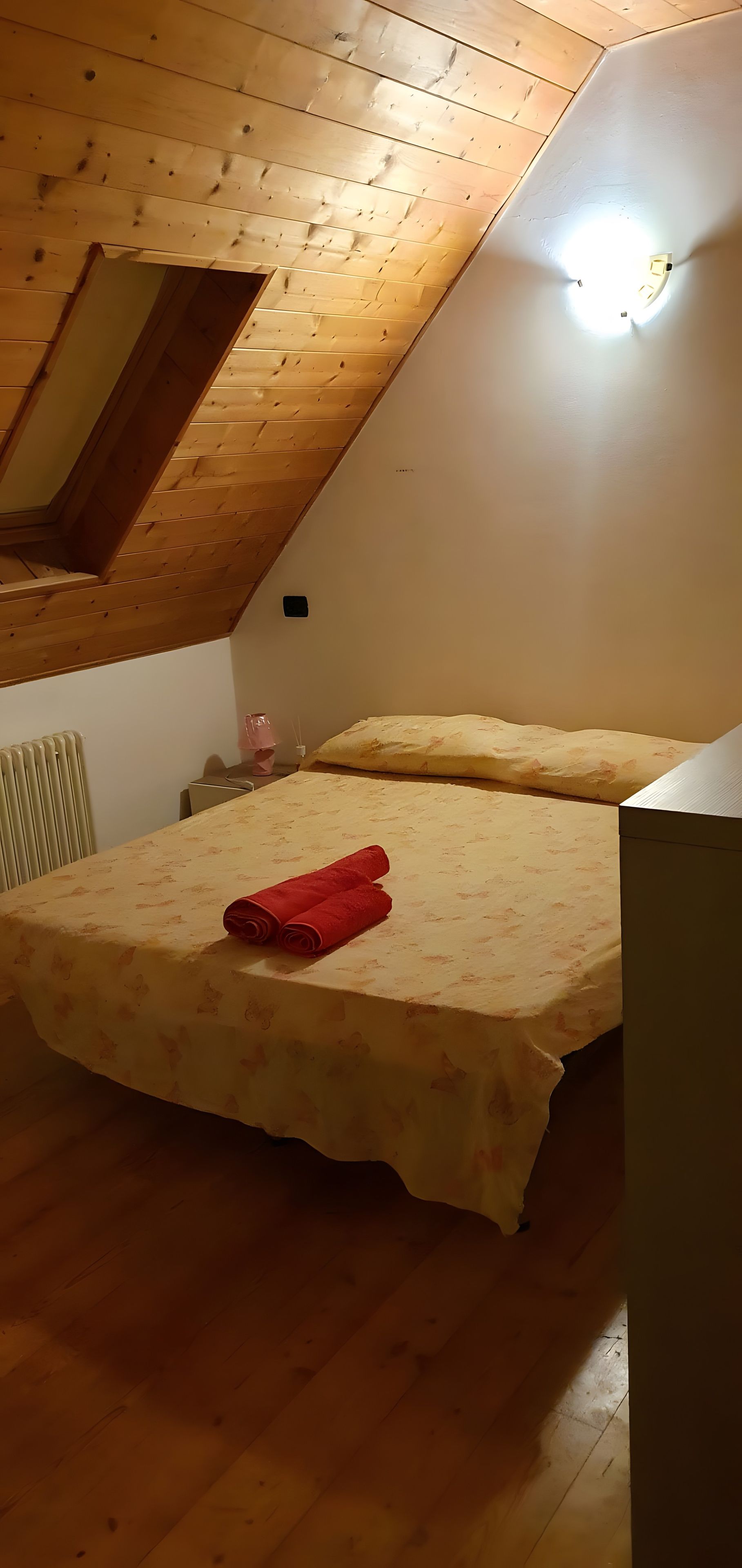 A room with a sloped ceiling, a bed with a floral bedspread, and a red towel on the bed.