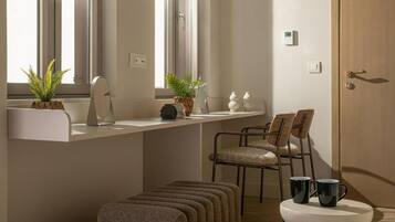 Une salle de bain moderne avec un meuble-lavabo blanc, deux plantes en pot, un miroir et des toilettes sur un socle blanc.