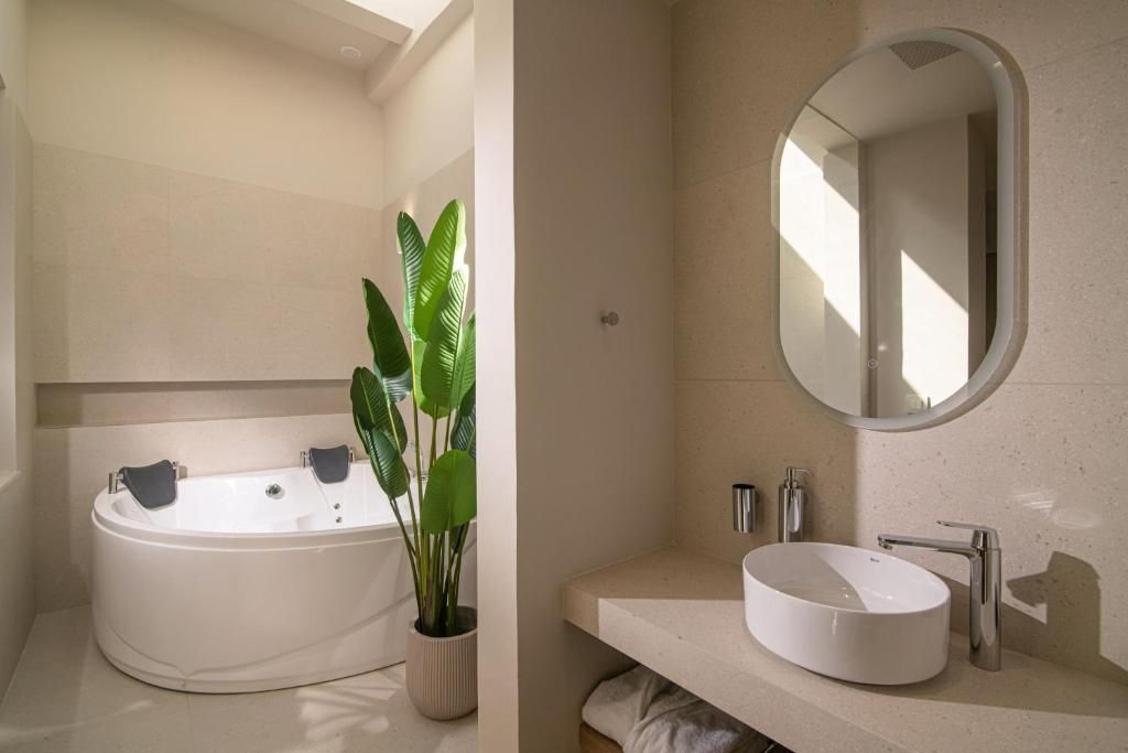 A modern bathroom with a freestanding bathtub, a round sink, a large mirror, and a potted plant.