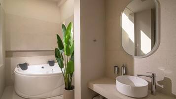 A modern bathroom with a freestanding bathtub, a round sink, a large mirror, and a potted plant.