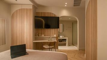 Une chambre moderne comprenant un lit, un bureau, une chaise, un téléviseur et une salle de bain visible à travers une arche.
