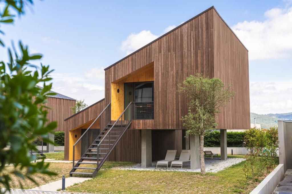 A modern building with a wooden exterior, a staircase leading to a balcony, and a small garden area with seating.