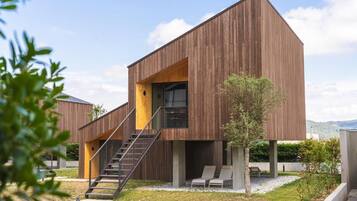 A modern building with a wooden exterior, a staircase leading to a balcony, and a small garden area with seating.