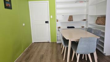 A room with a wooden floor, a white door, a table with chairs, and a white shelving unit with baskets.