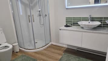 A bathroom with a glass-enclosed shower, a white sink, and a green-tiled backsplash.