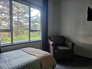 A room with a bed, a chair, and a window with a view of trees and a path. - Hokio Hideaway | Private 2-Bedroom Rural Guest Wing | Sleeps up to 6 (Hokio Beach)