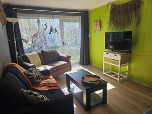 A living room with a sofa, a coffee table, a TV on a stand, and a large window with curtains. - Hokio Hideaway | Private 2-Bedroom Rural Guest Wing | Sleeps up to 6 (Hokio Beach)