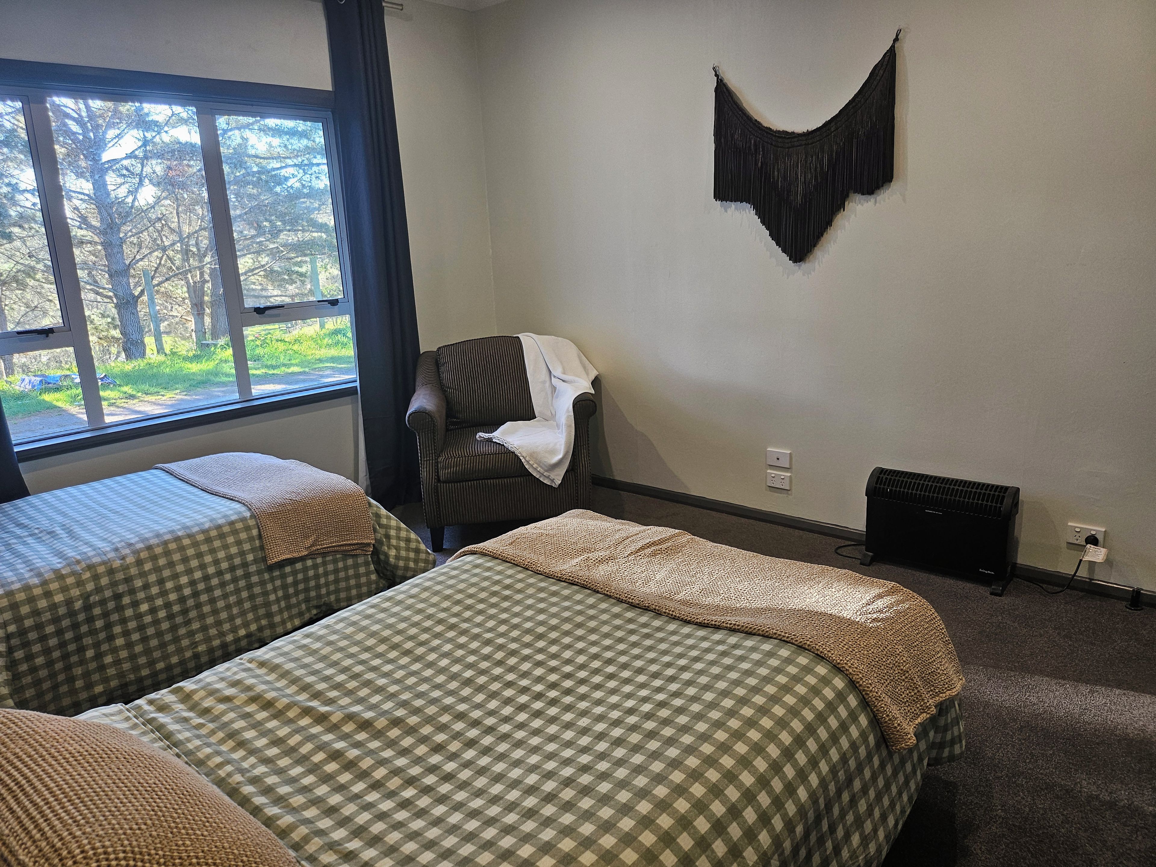 A room with two beds, a chair, a wall-mounted decoration, and a radiator.