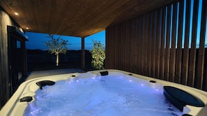 A hot tub with a wooden ceiling and walls, surrounded by a wooden fence.