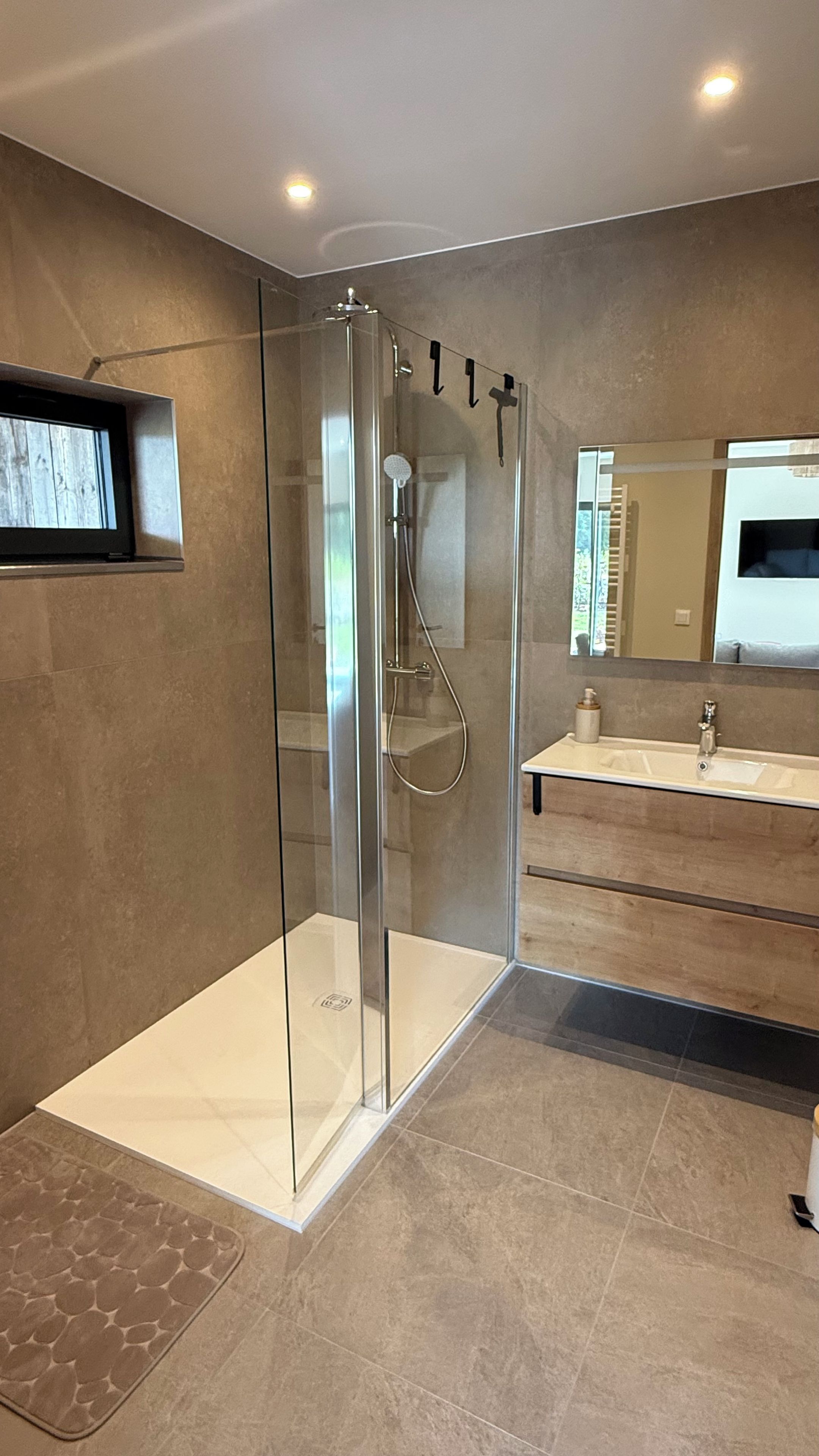 Een moderne badkamer met een douchecabine van glas, een wastafel met spiegel en een betegelde vloer.